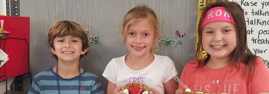 Three students from Westchester Elementary School smiling and holding up ice cream sundaes.